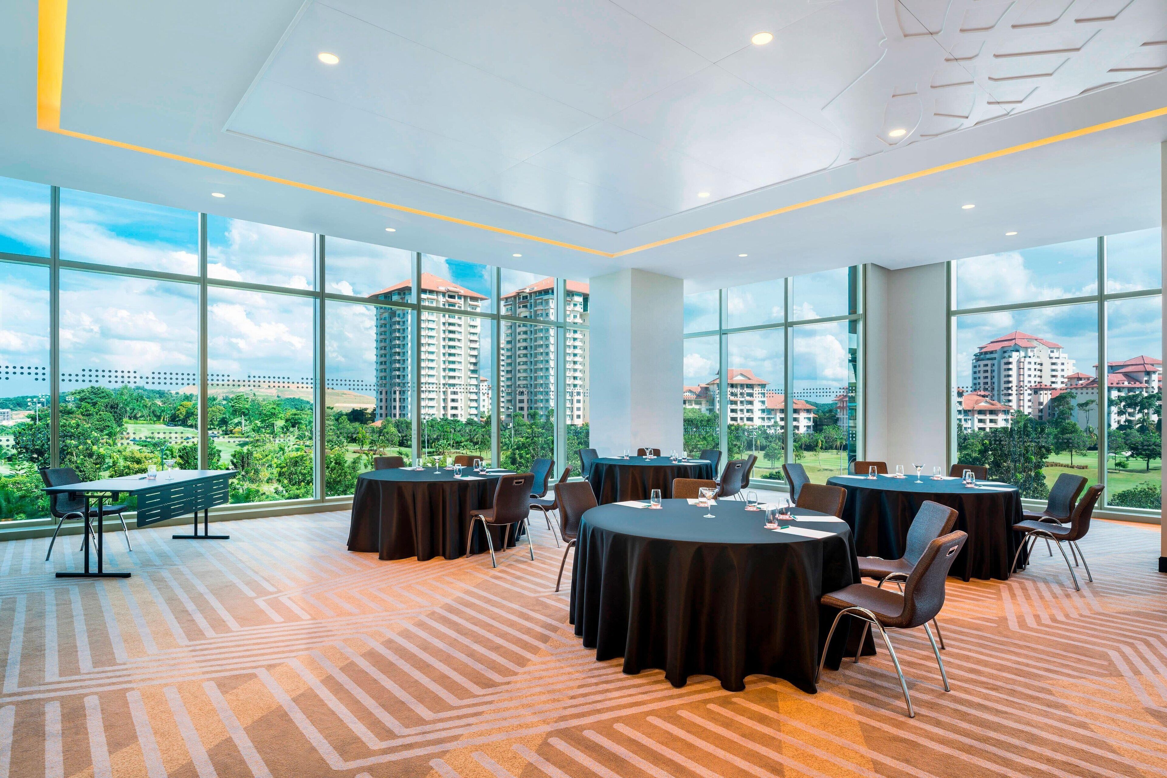 Une salle de conférence dotée de grandes fenêtres, de tables rondes et de chaises, offrant une vue sur le paysage urbain.