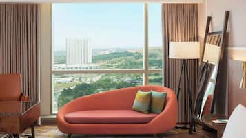 A hotel room with a large window, a sofa, a chair, a bed, and a lamp.