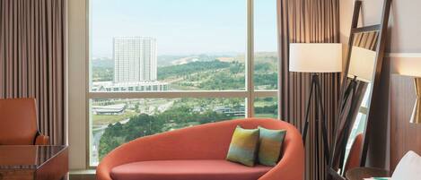 A hotel room with a large window, a sofa, a chair, a bed, and a lamp.