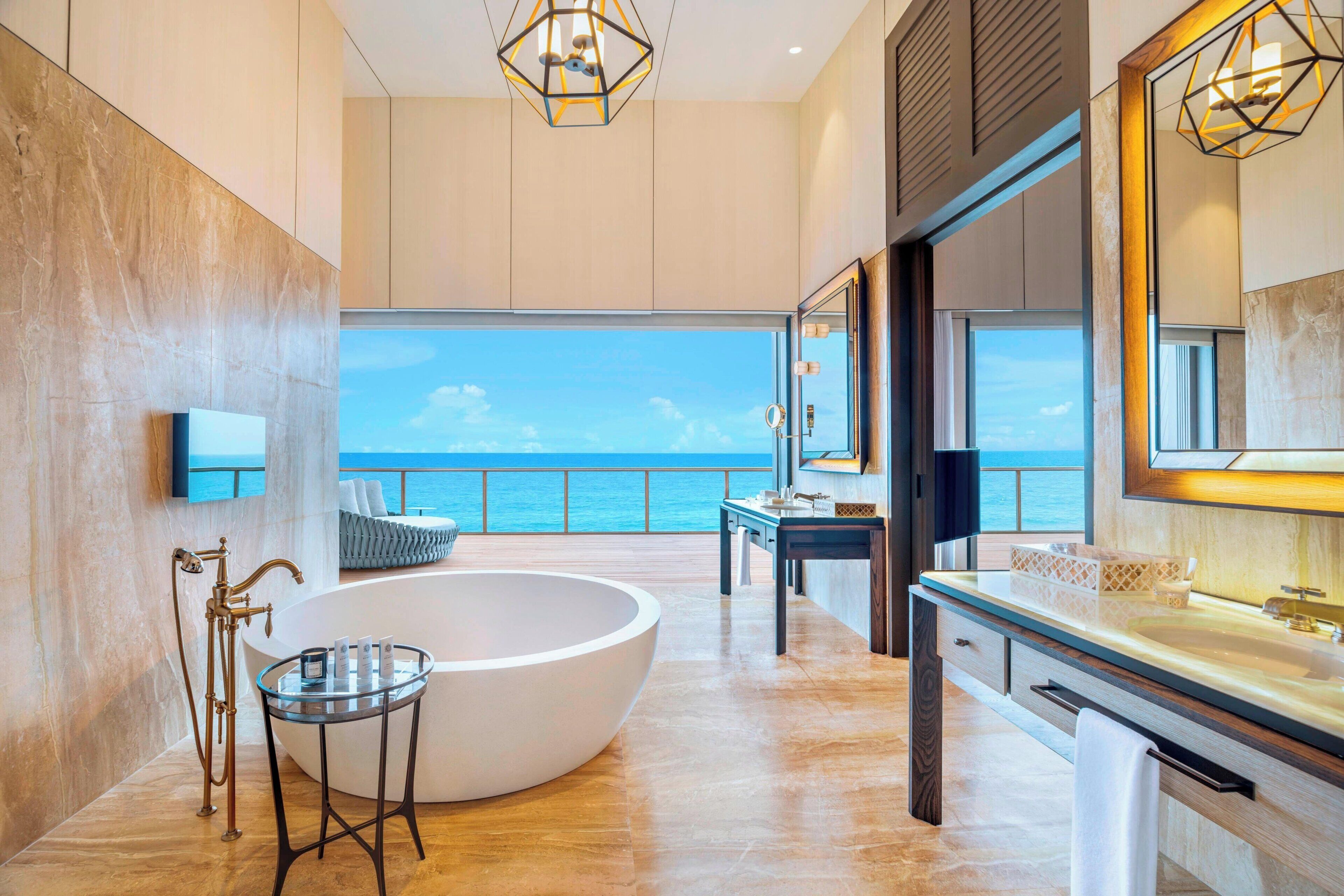 A modern bathroom with a large bathtub, a glass table, and a view of the sea.