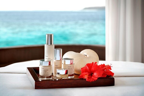 A tray with skincare products and a red flower on a bed with a view of the ocean.