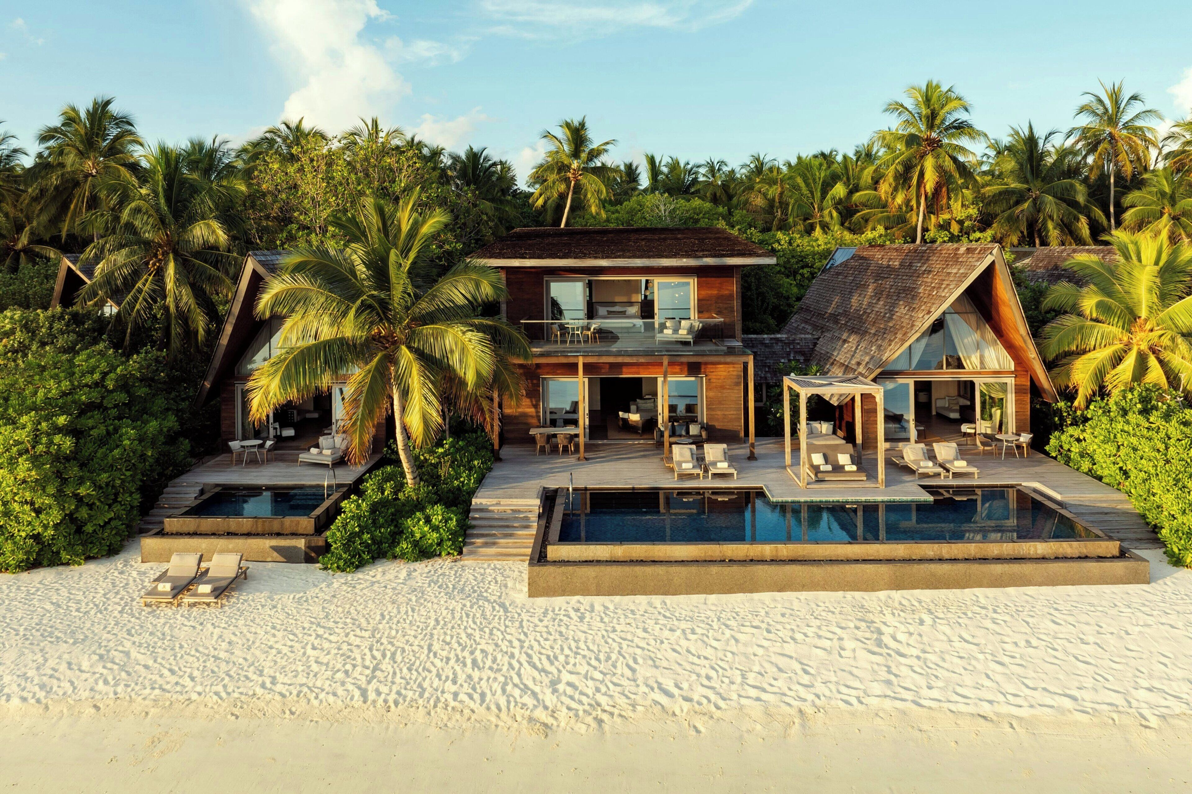 A modern beachfront property with a pool, outdoor seating, and lush tropical surroundings.