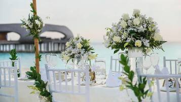 Decoración de boda en la playa, con sillas blancas, cristalería y centros de mesa florales.