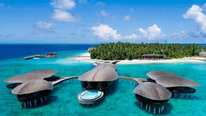 Overwater bungalows with thatched roofs, a pool, and a view of the ocean and a tropical island. - The St. Regis Maldives Vommuli Resort (Vommuli)