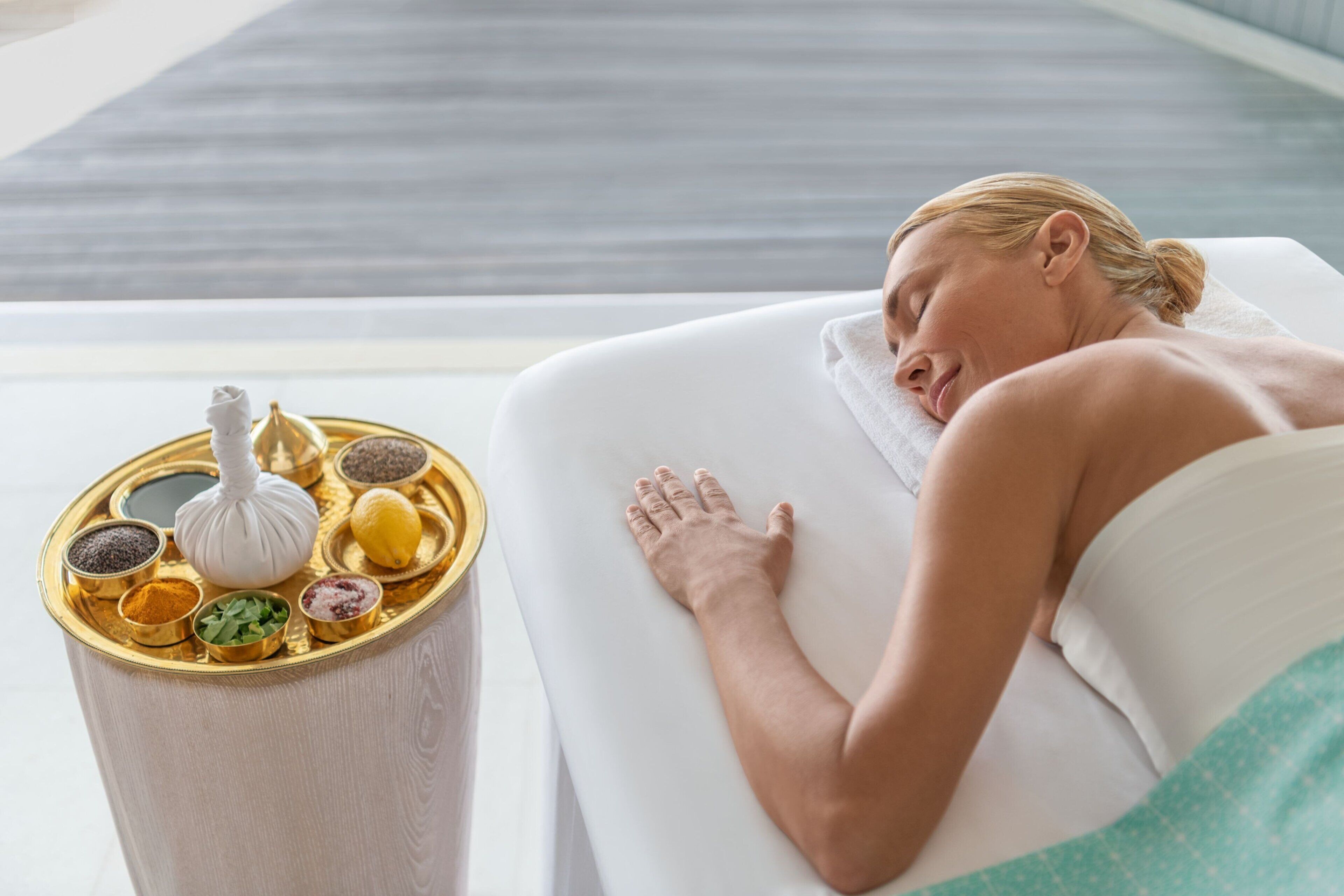 A spa setting with a massage table, a decorative container with various items, and a view of a modern interior.