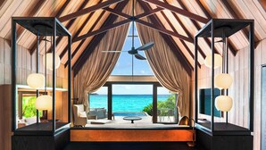 A modern room with a large window overlooking the sea, a ceiling fan, and a seating area with a table and chairs. - The St. Regis Maldives Vommuli Resort (Vommuli)