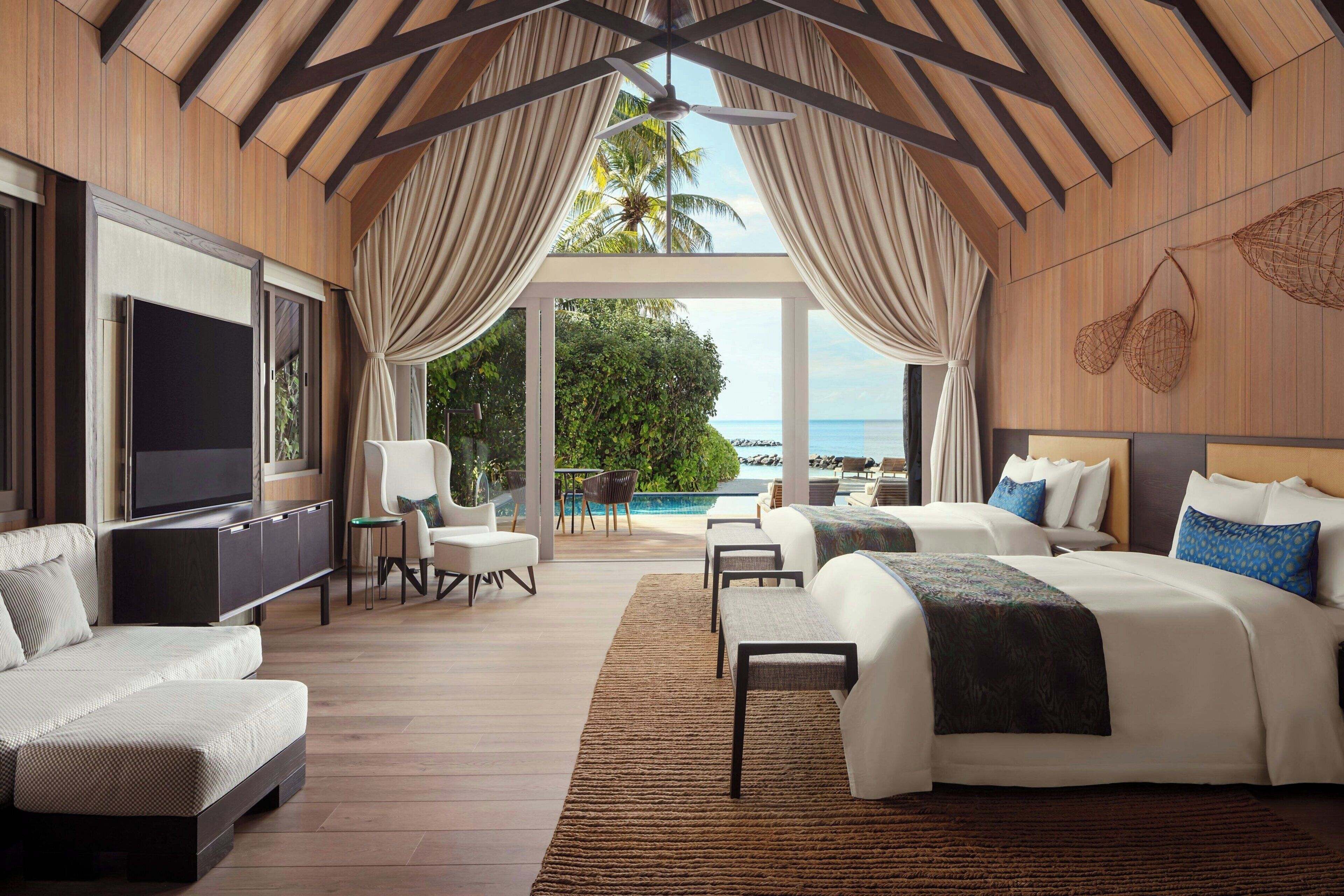 A spacious room with a large bed, a TV, a seating area with a table, and a view of the ocean.