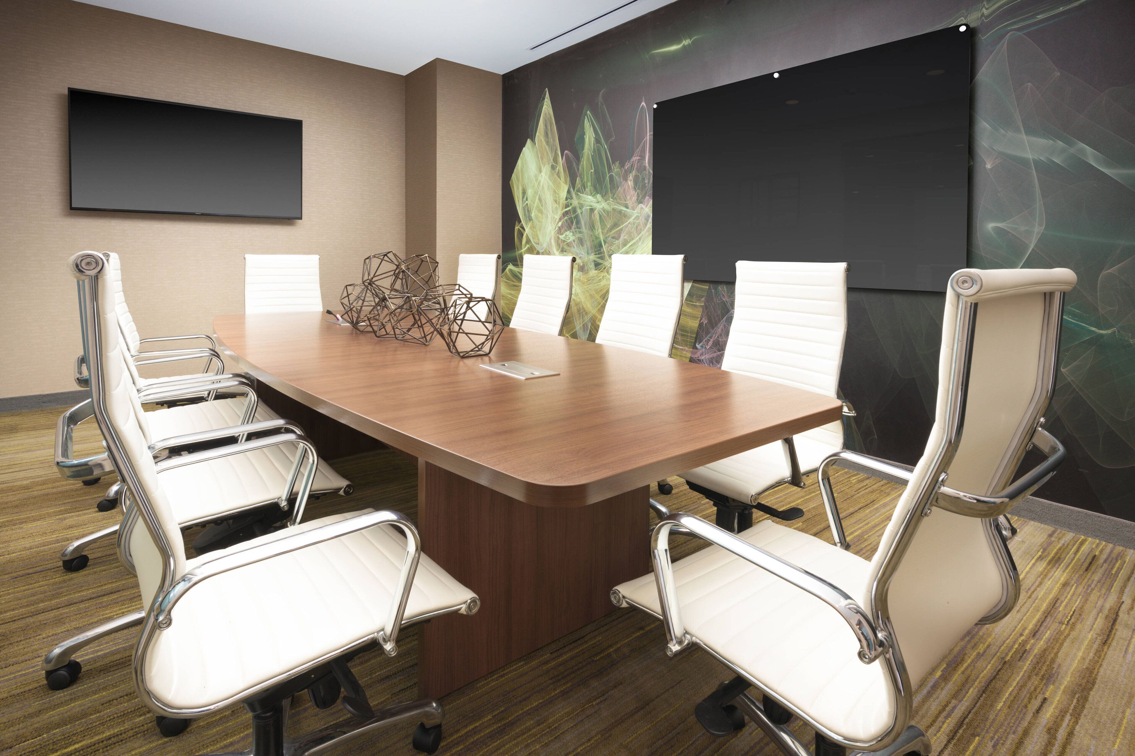 A conference room with a large wooden table, six white chairs, a projector screen, and a large plant.