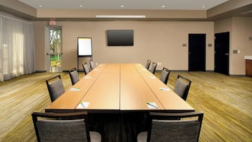 A conference room with a long table, chairs, a projector screen, and a door with an exit sign.