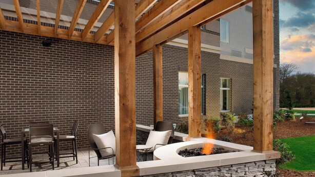 An outdoor patio with a fire pit, wooden pergola, and seating area against a brick wall.