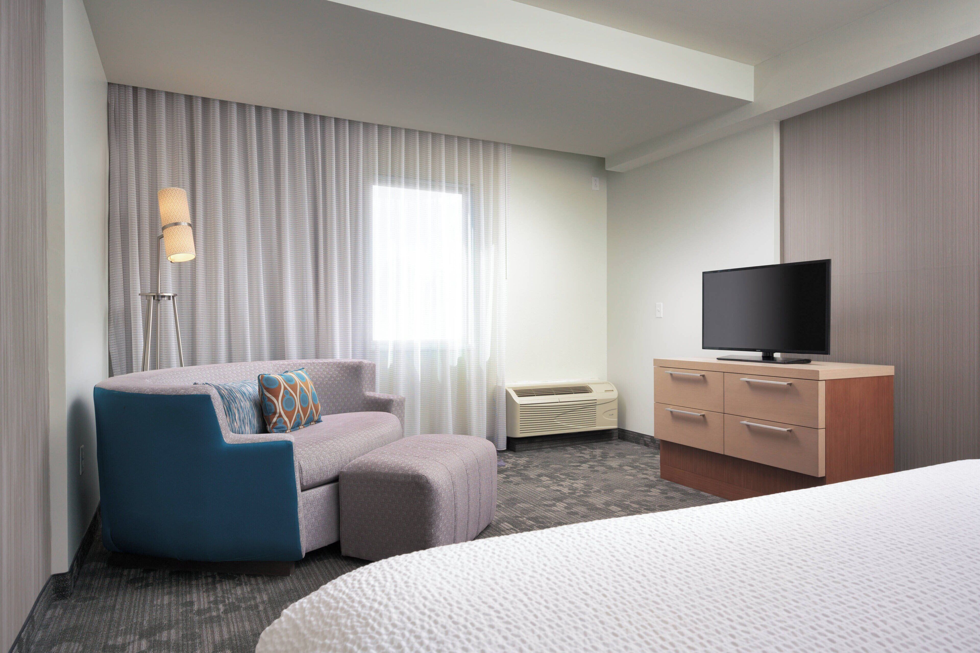 A hotel room with a bed, a sofa, a TV, a dresser, and a window with curtains.