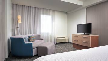 A hotel room with a bed, a sofa, a TV, a dresser, and a window with curtains.