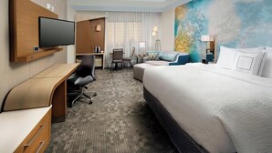 A hotel room with a large bed, a desk, a chair, a television, and a painting on the wall.