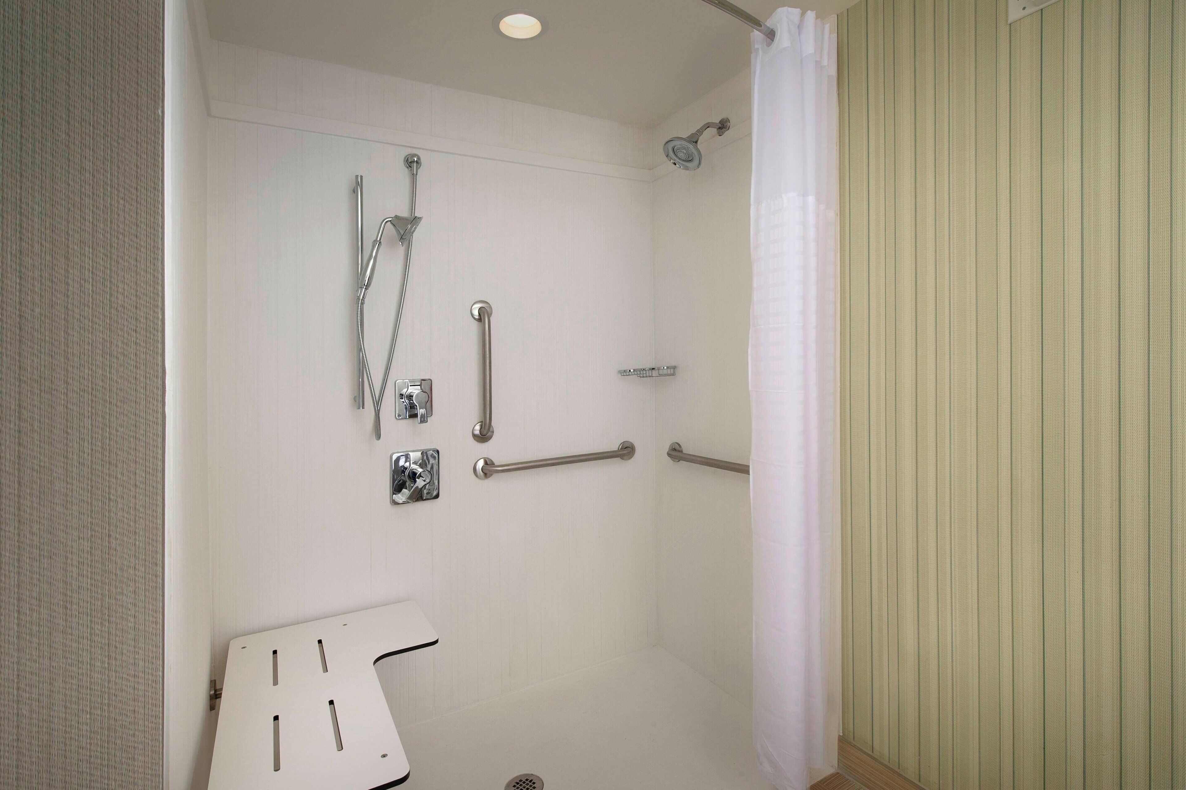 A shower with grab bars, a handheld showerhead, and a shower control panel.