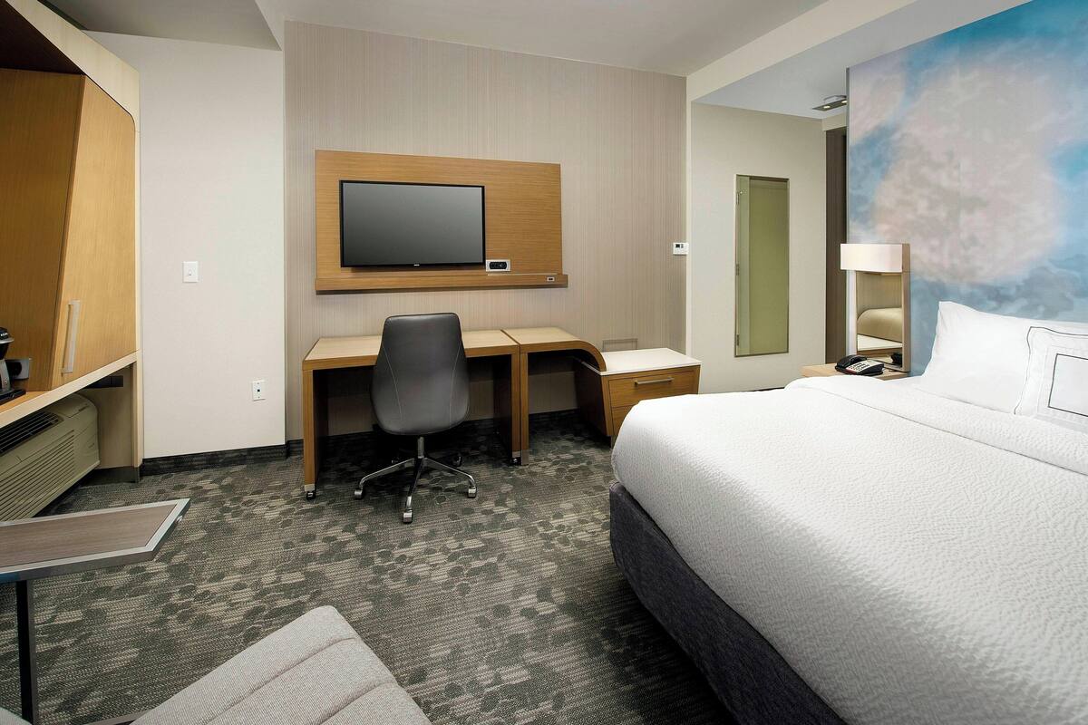 Une chambre d’hôtel comprenant un lit, un bureau avec une chaise, un téléviseur fixé au mur et un tableau accroché au mur.