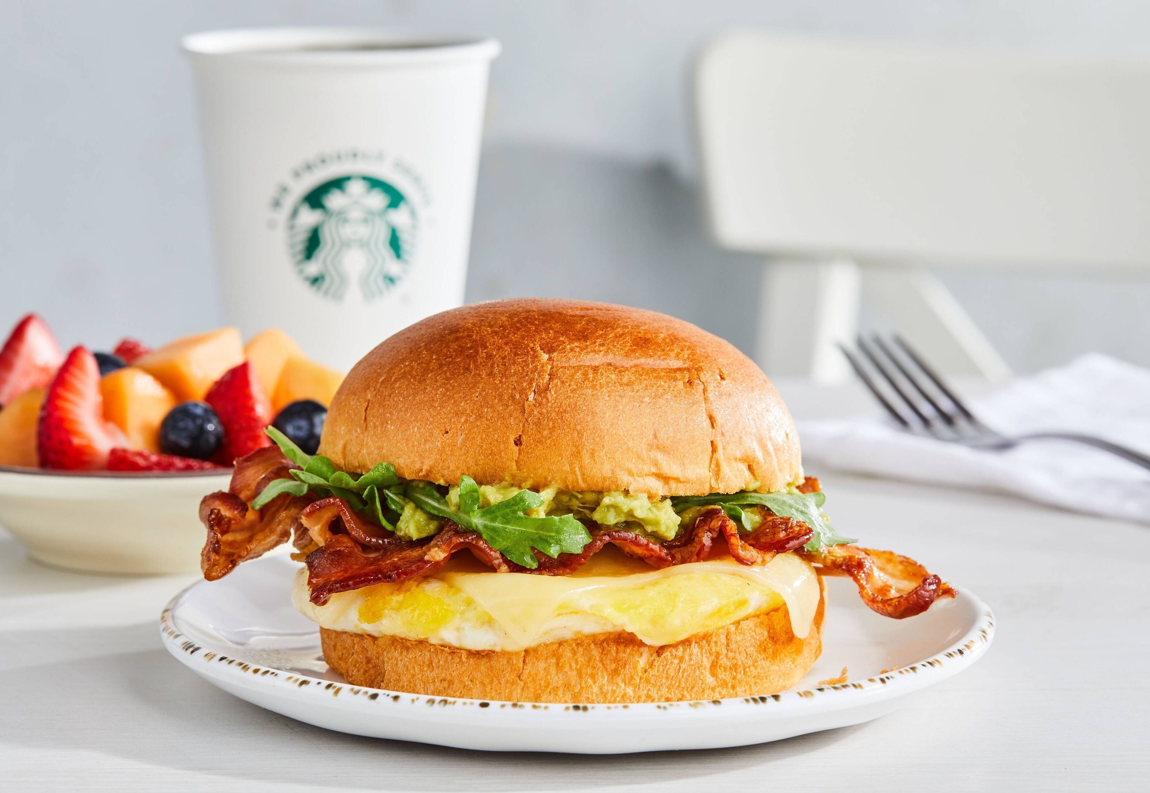 A breakfast sandwich on a plate with a cup of coffee in the background.