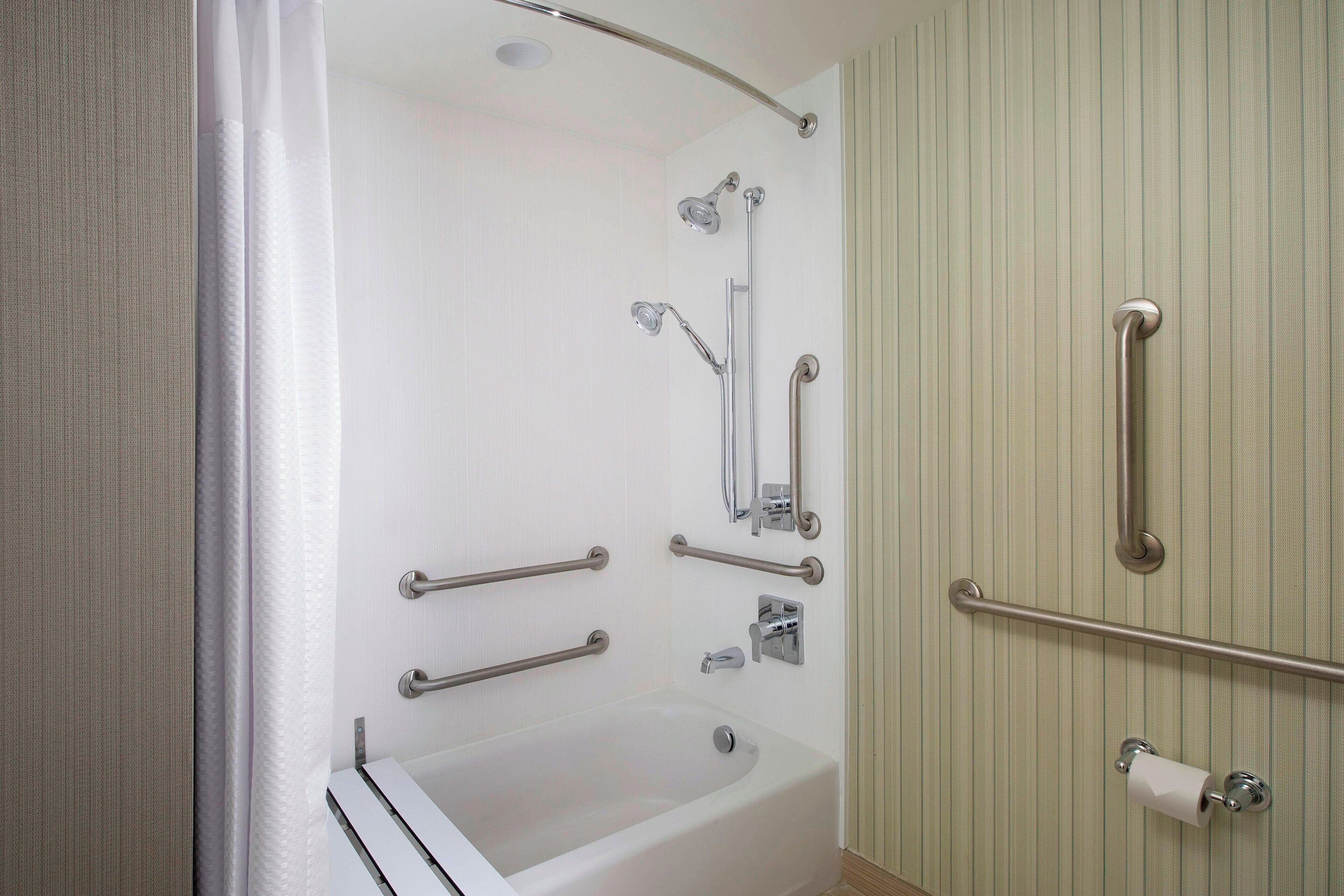 A bathroom with a bathtub, grab bars, a showerhead, and a toilet paper holder.