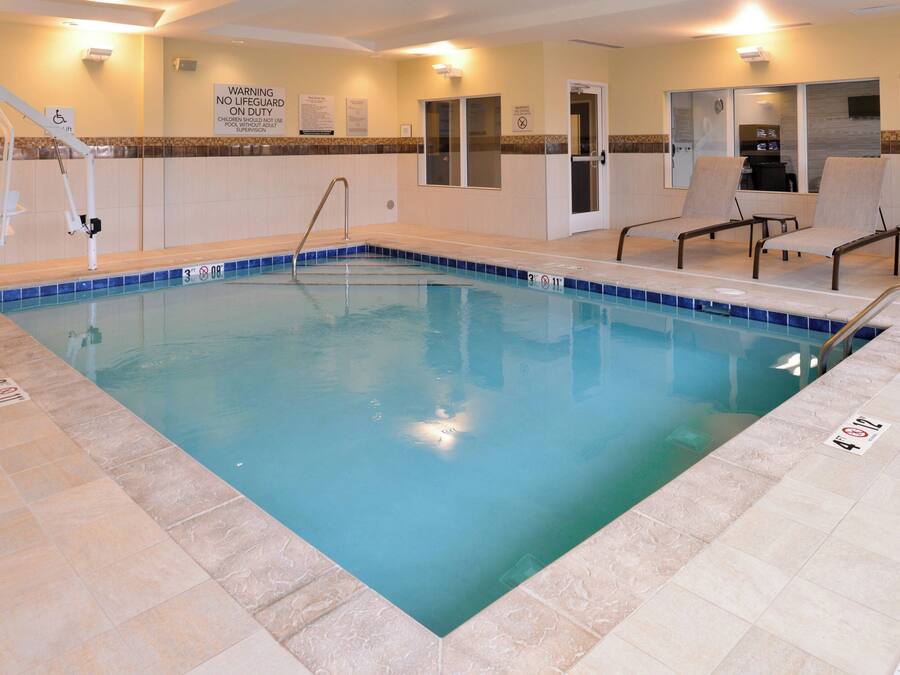Una piscina interior con una silla de salvavidas, sillas de descanso y un cartel que indica que no hay salvavidas de servicio.