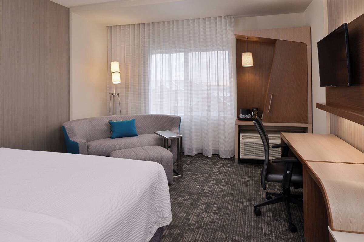 A hotel room with a large bed, a sofa, a desk, a chair, and a TV.