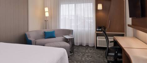 Una habitación de hotel con una cama grande, un sofá, un escritorio, una silla y un televisor.