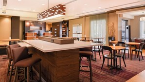 A modern hotel lobby with a central bar area, seating arrangements, and a reception desk.