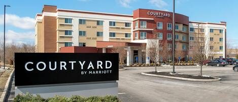 Un hotel Courtyard by Marriott con un letrero en la entrada, un estacionamiento y cielo despejado.