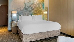 A hotel room with a large bed, a nightstand with a lamp, and a wall with a textured abstract design.