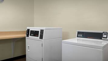 A laundry room with two white commercial washers and dryers, a wooden countertop, and a wall clock.