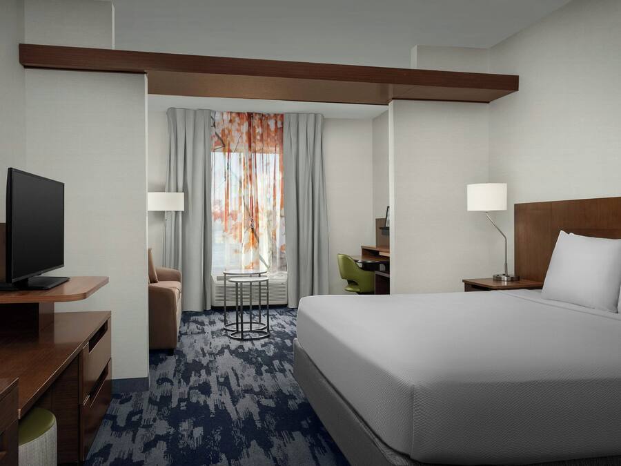 A hotel room with a large bed, a desk with a TV, a small table, and a chair.
