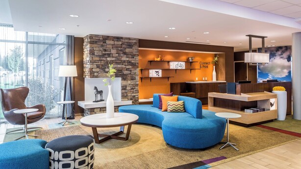 A modern hotel lobby with a stone accent wall, a blue sofa, a round coffee table, and a reception desk. - Fairfield Inn & Suites by Marriott Butte (Butte)