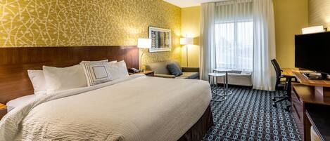 A hotel room with a large bed, a desk with a TV, a chair, and a window with curtains.