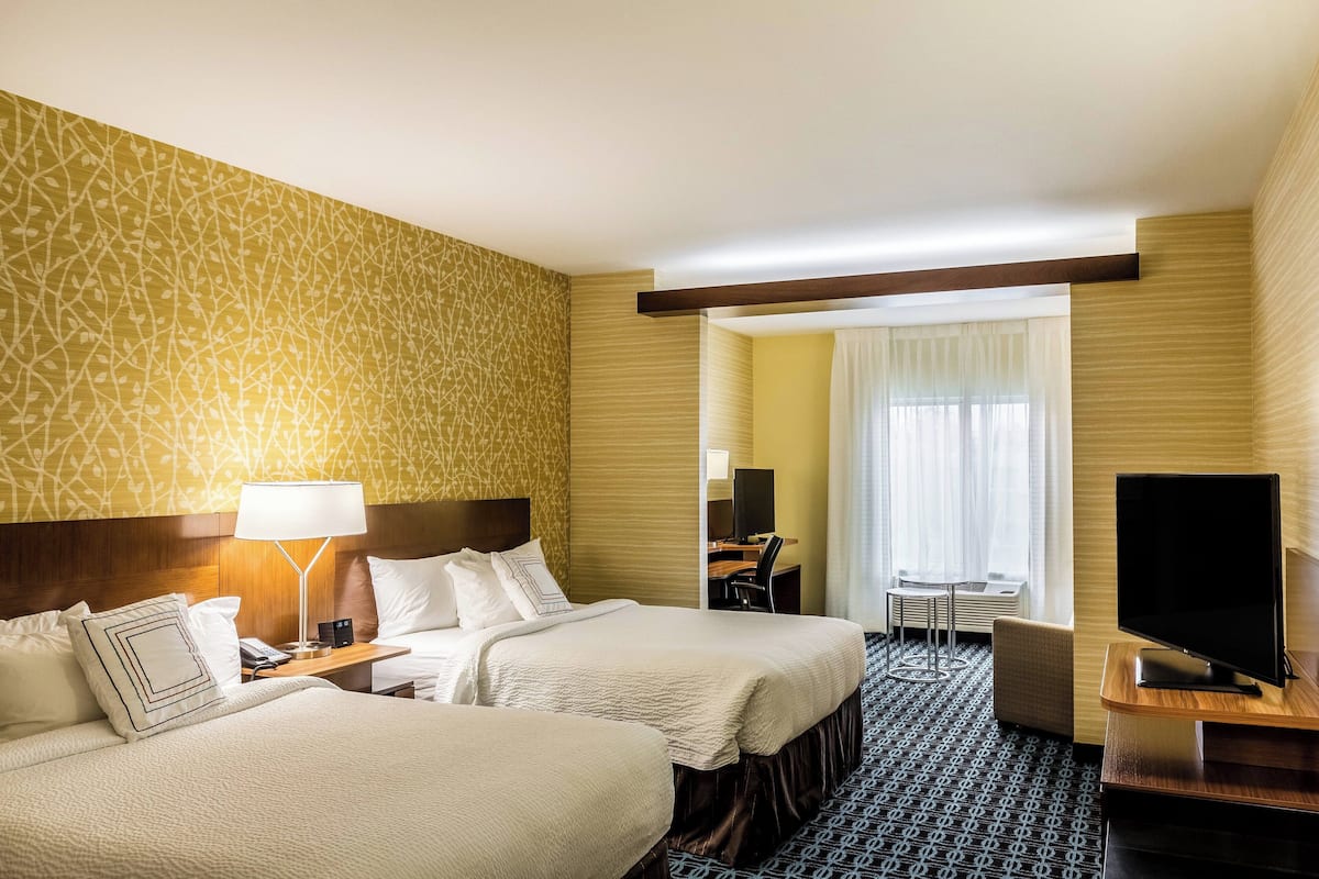 A hotel room with two beds, a desk, a chair, a TV, and a window with curtains.