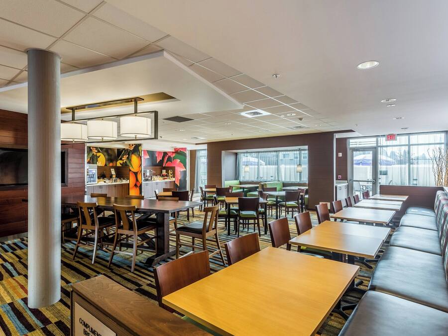 Een moderne eetruimte met meerdere tafels en hoekbanken, een grote pilaar en een uitzicht naar buiten door grote ramen.