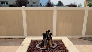 A square stone fire pit with a central wood feature, surrounded by a beige fence and set on a concrete patio. - Fairfield Inn & Suites by Marriott Butte (Butte)