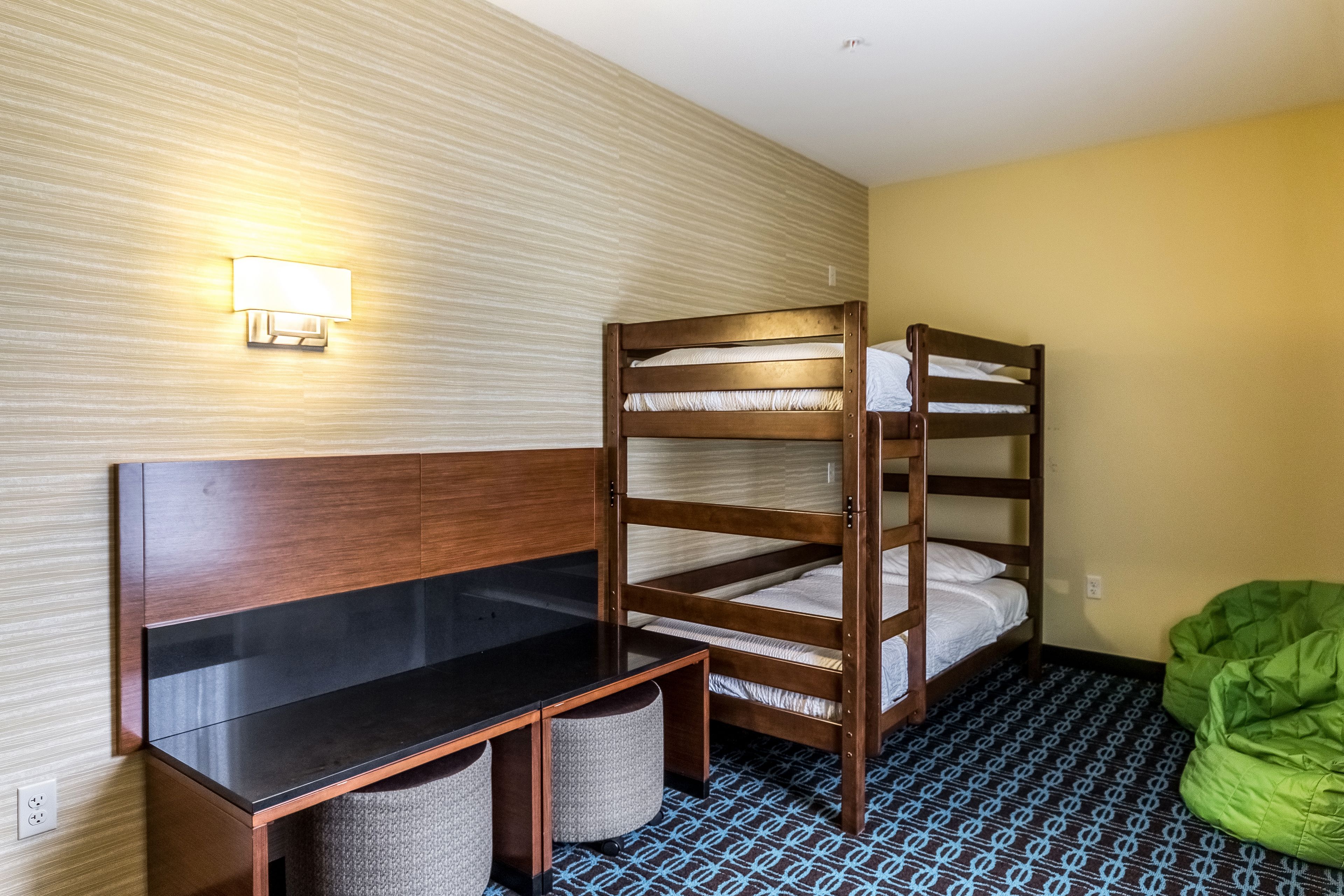 A bunk bed with a desk and two chairs, a wall-mounted light, and a green bean bag chair.