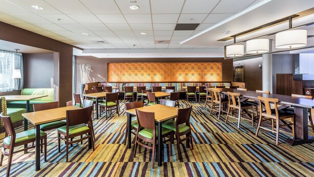 A hotel dining area with multiple tables and chairs, a patterned carpet, and a modern ceiling design.