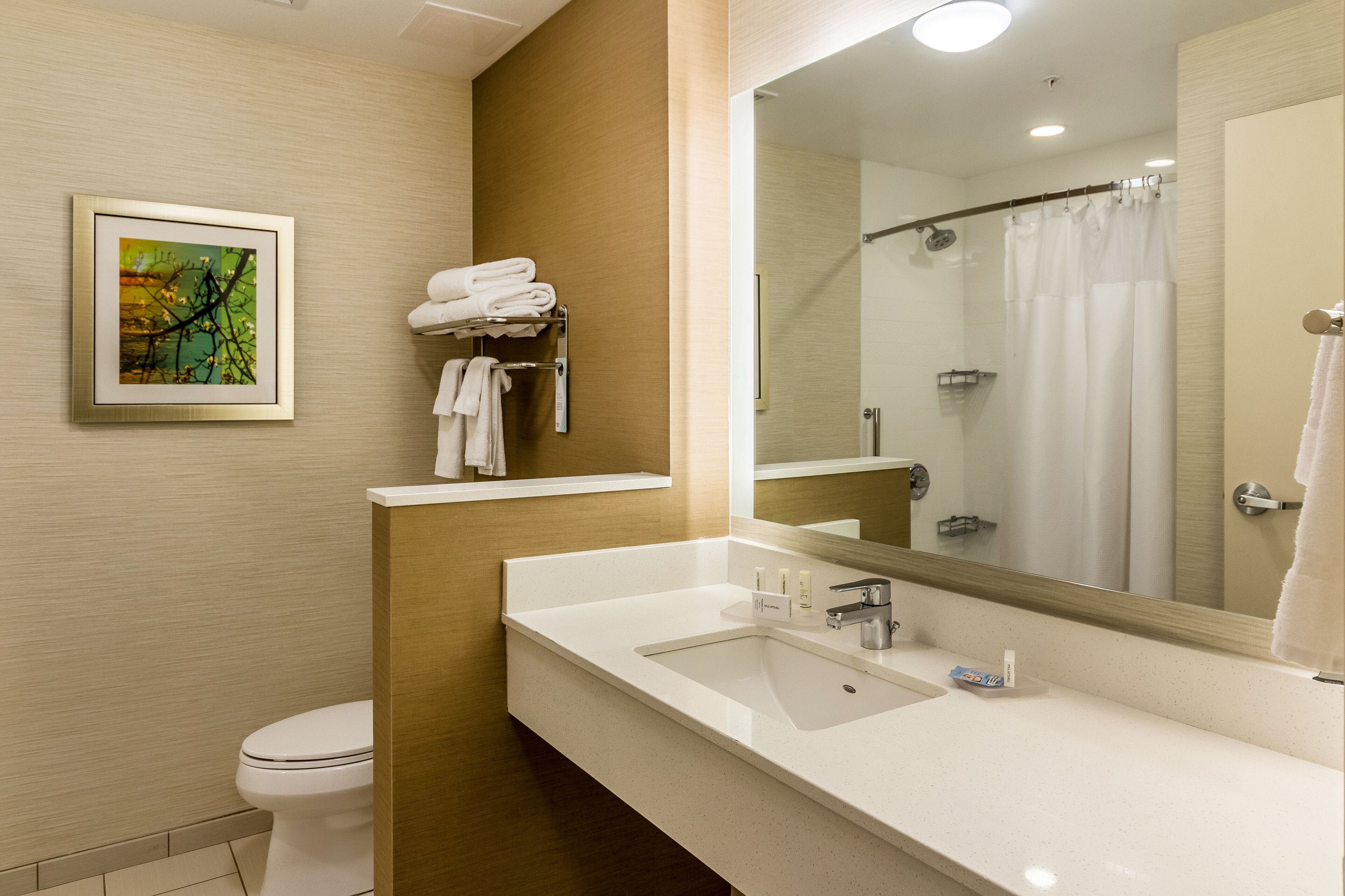 A modern bathroom with a white sink, a large mirror, a shower with a glass door, and a towel rack with folded towels.