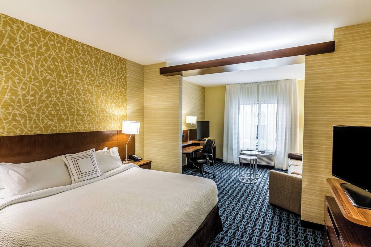 A hotel room with a large bed, a desk with a chair, a television, and a small table with a chair.