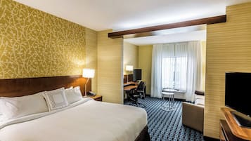 Habitación de hotel con una cama grande, un escritorio con silla, un televisor y una pequeña mesa con otra silla.