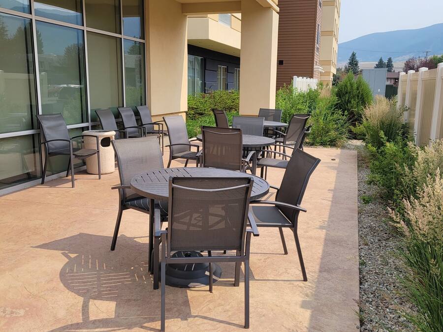 Una terrazza esterna con tavoli e sedie, circondata da un edificio con ampie finestre e vista sulle montagne.