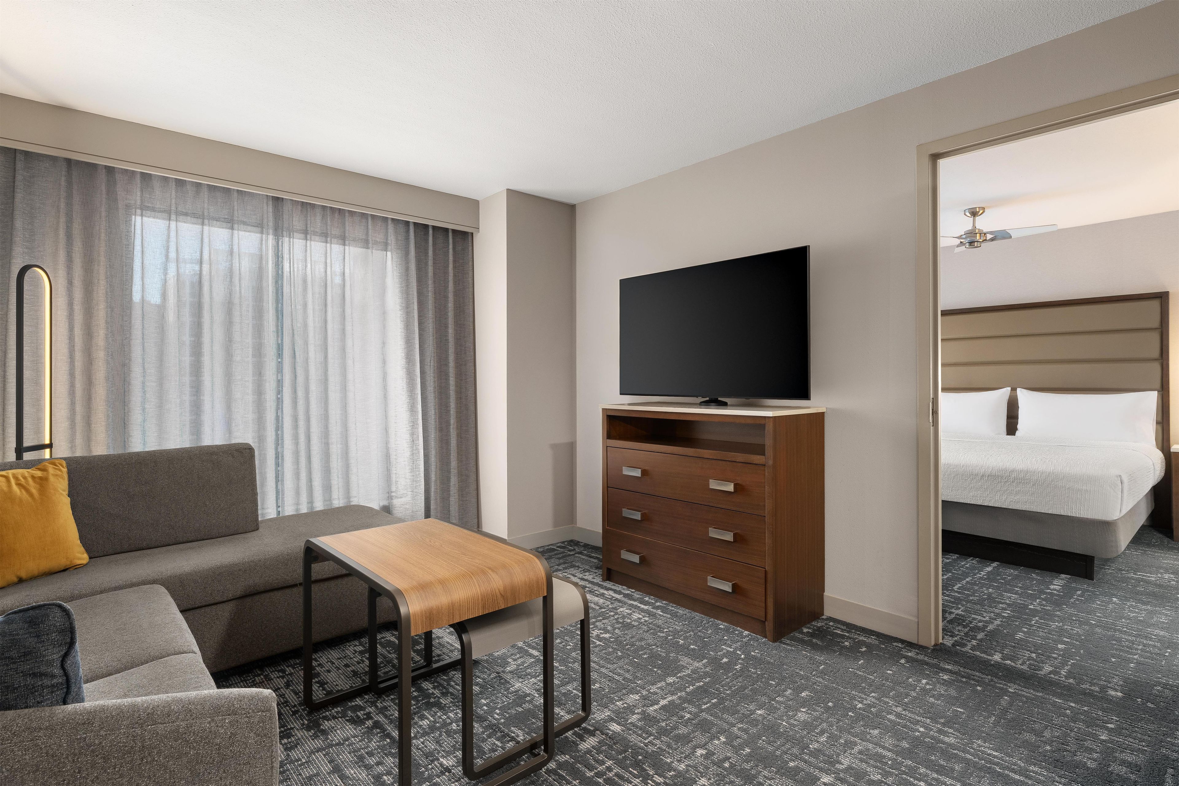 Een hotelkamer met een bank, een houten salontafel, een televisie op een standaard, een bed en een kledingkast.