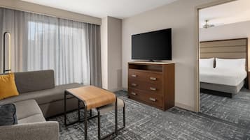 Een hotelkamer met een bank, een houten salontafel, een televisie op een standaard, een bed en een kledingkast.