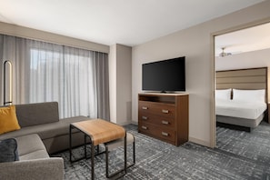 Une chambre d’hôtel avec un canapé, une table basse en bois, un téléviseur posé sur un meuble, un lit et une armoire.