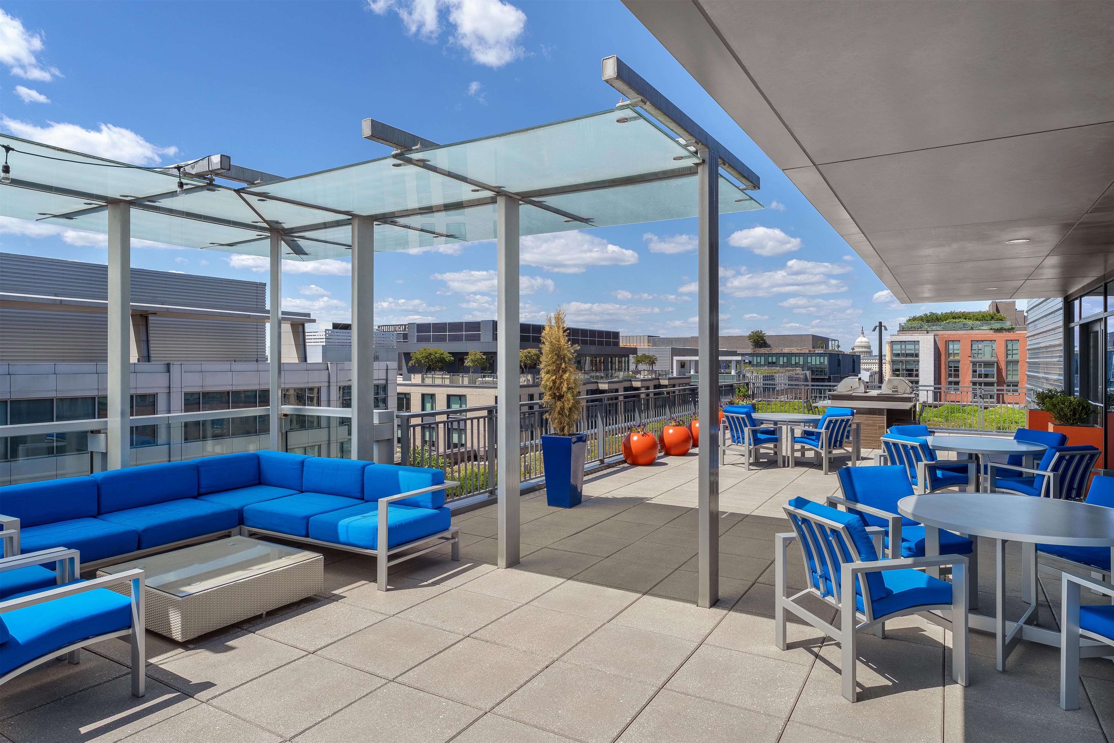 A rooftop patio with blue seating, glass panels, and a view of buildings.