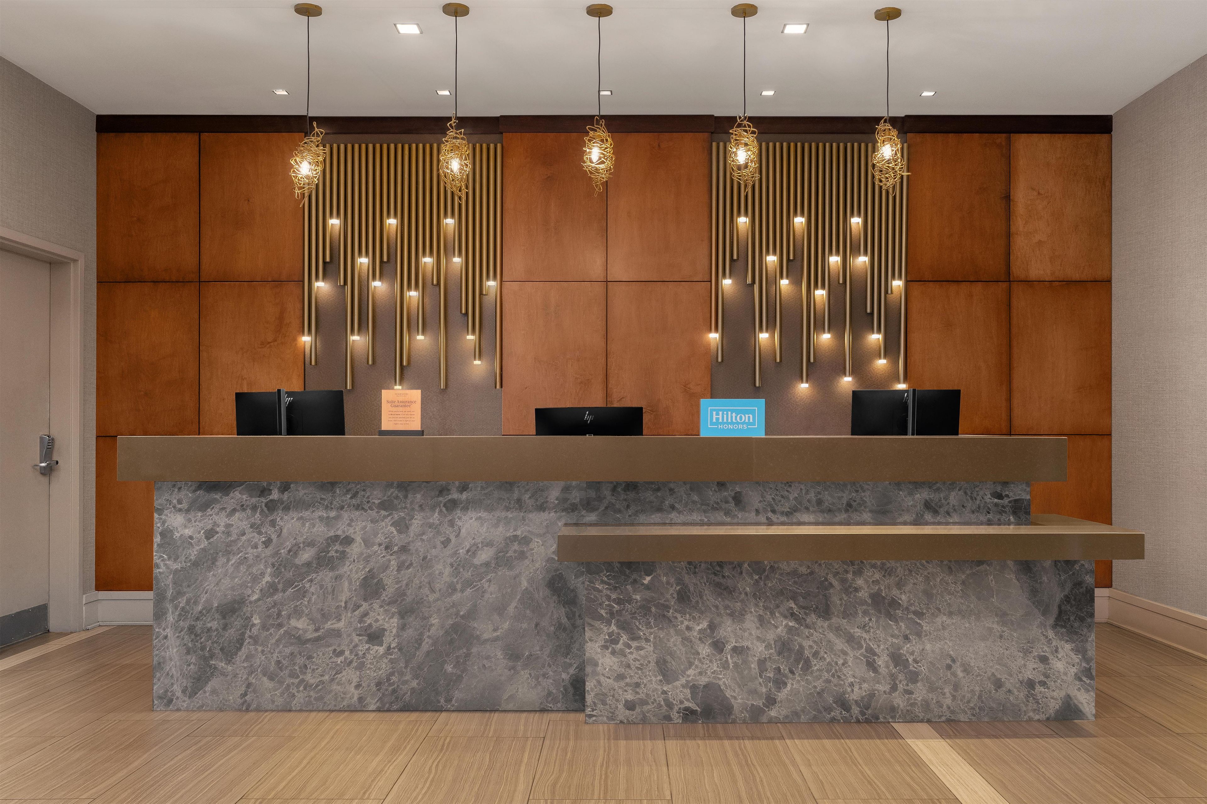 A hotel reception desk with a marble counter, two black chairs, and a sign indicating Hilton branding.