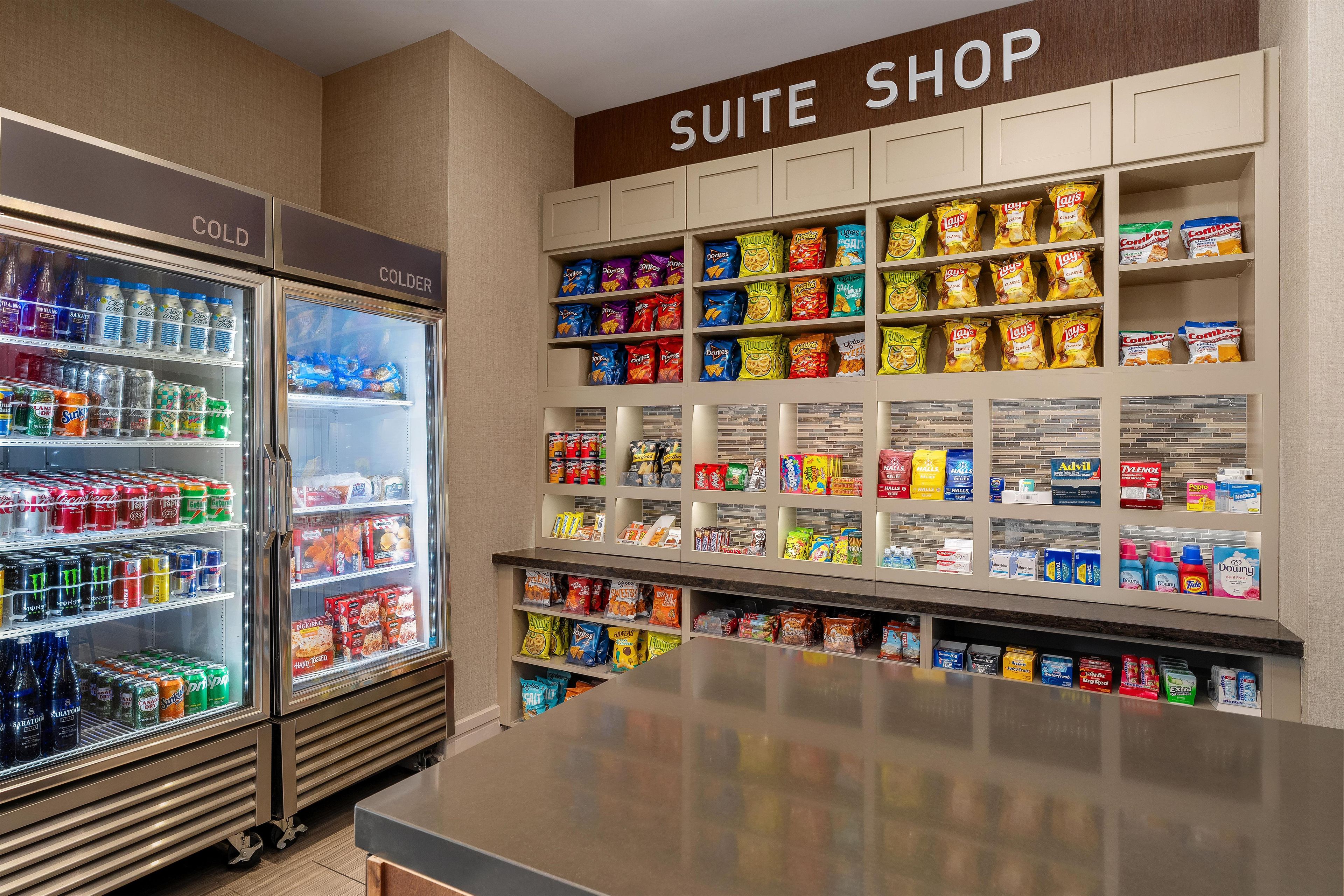 A hotel suite shop with refrigerated beverage cases and shelves stocked with snacks and toiletries.