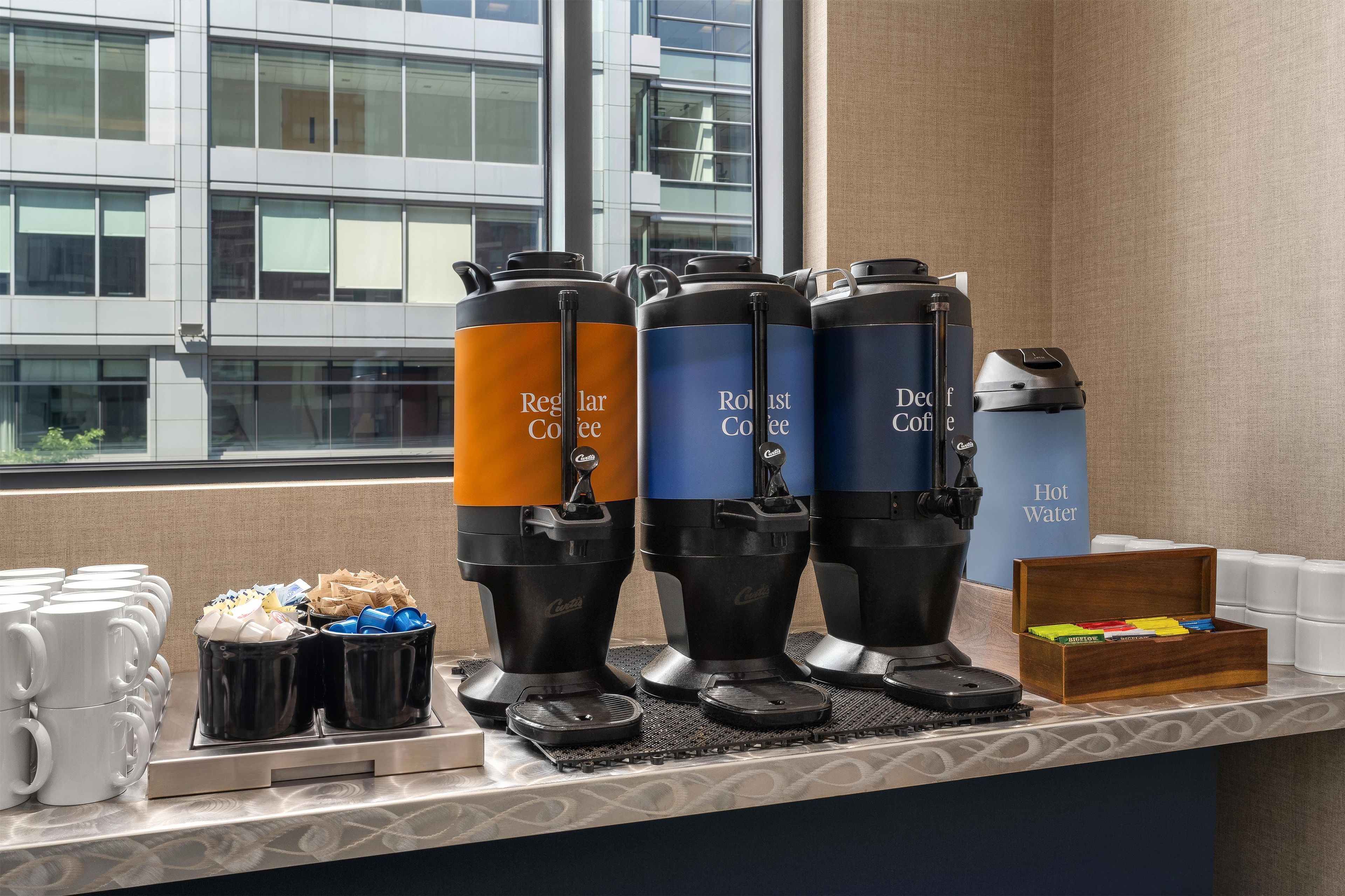 Un espace dédié au café, équipé de distributeurs étiquetés « Café ordinaire », « Café en grains » et « Café décaféiné », ainsi qu’un distributeur d’« eau chaude » et une boîte de capsules de café.