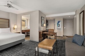 Una habitación de hotel con cama, escritorio, silla y un cuadro grande.