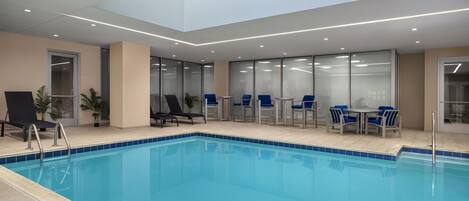 Una piscina interior moderna con paredes de vidrio transparente, sillas azules y tragaluces.