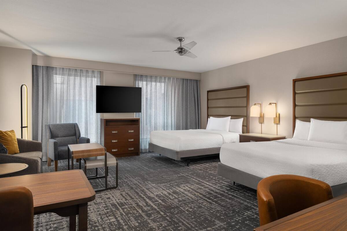 Una habitación de hotel con cama, escritorio, silla, televisor y ventilador de techo.